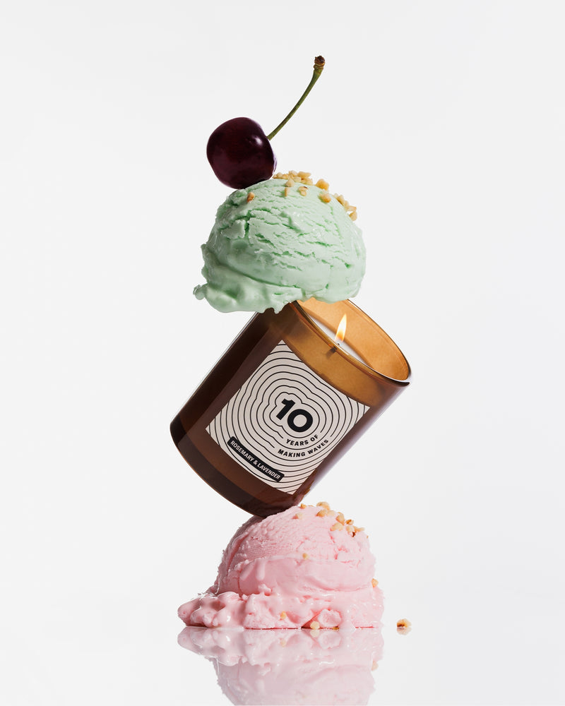 Una vela marrón equilibrada entre dos bolas de helado pastel, coronada con una cereza.