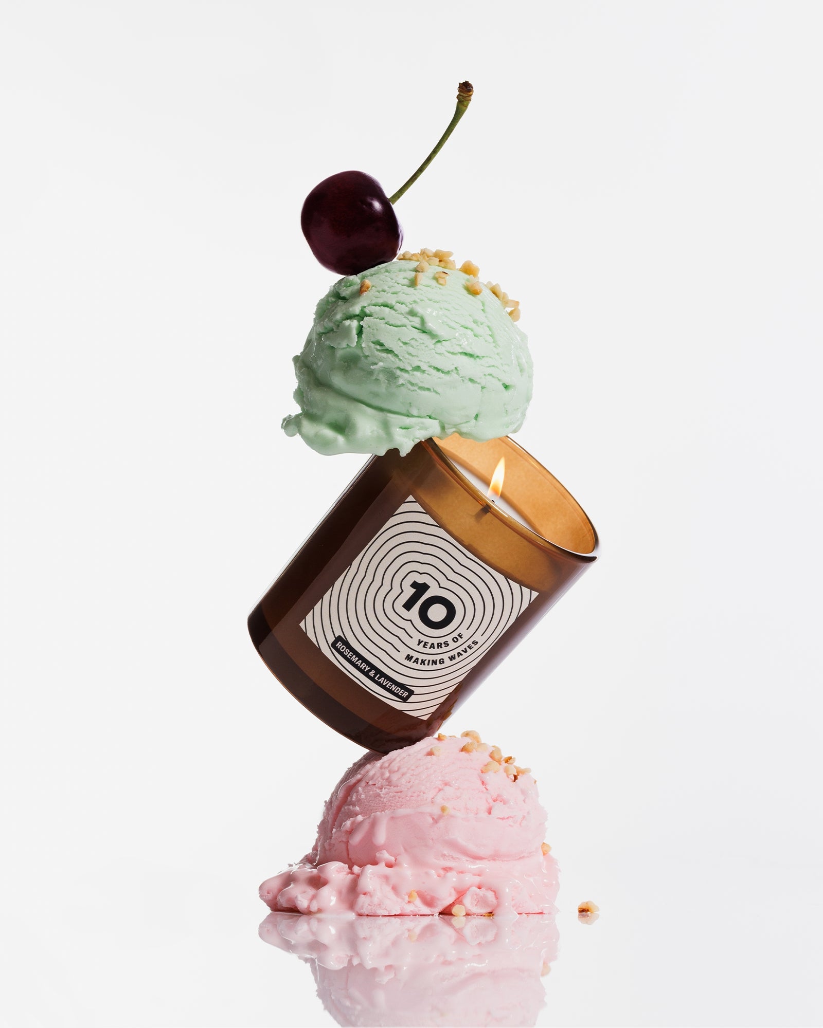 Una vela marrón equilibrada entre dos bolas de helado pastel, coronada con una cereza.