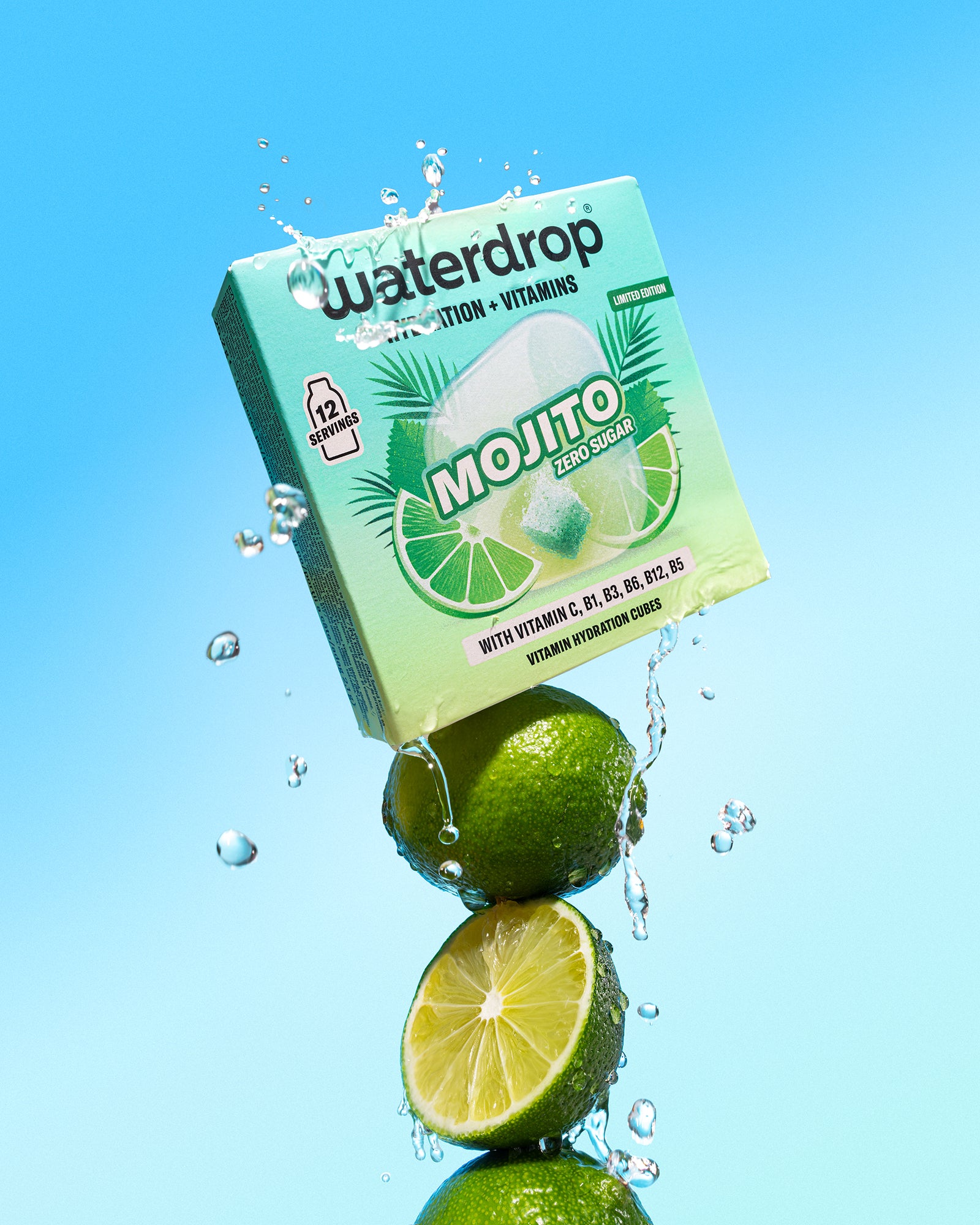 Limones apilados bajo una caja verde menta de bebida con salpicaduras de agua sobre fondo azul.