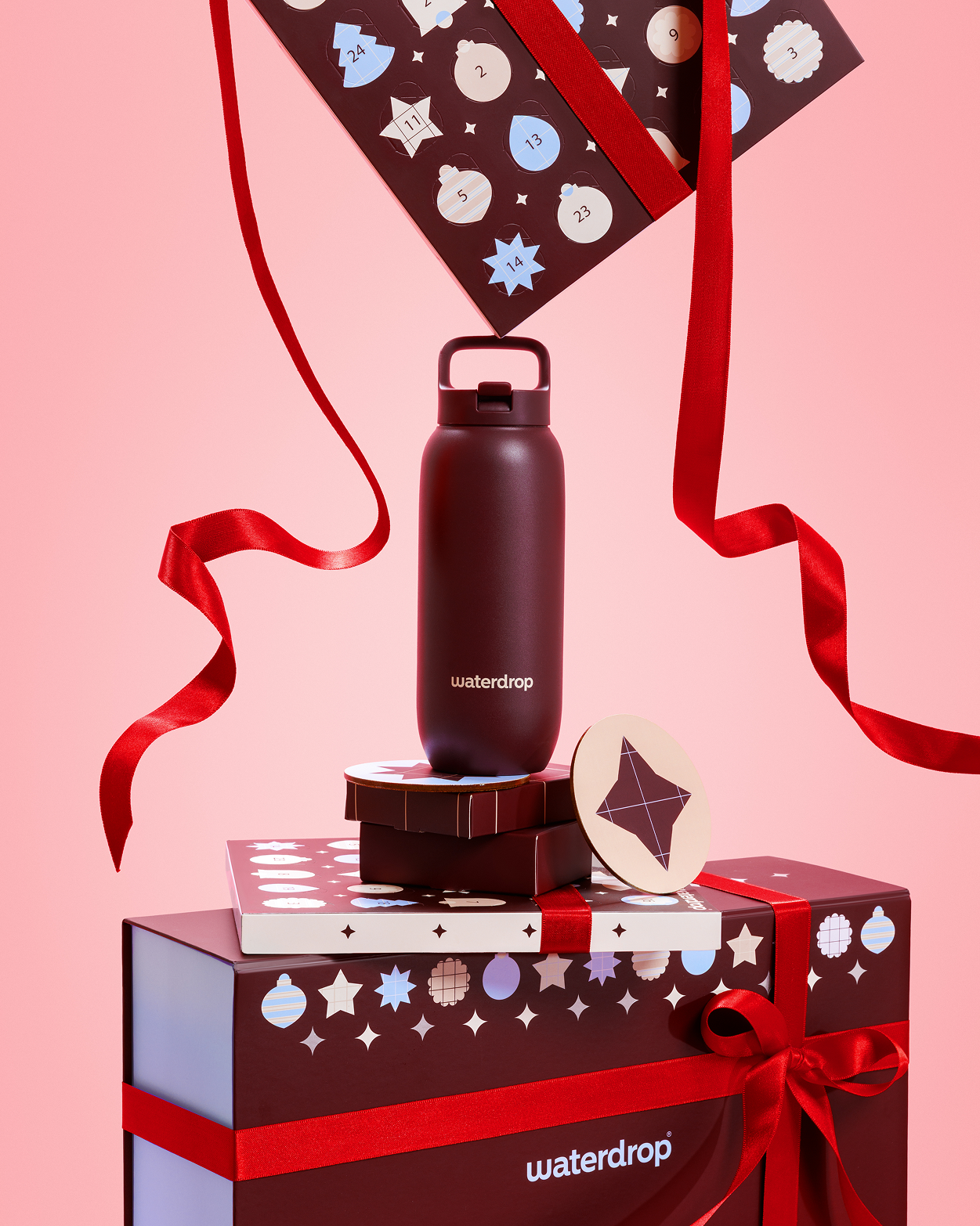 Botella oscura sobre cajas de regalo con lazos rojos y fondo rosa.