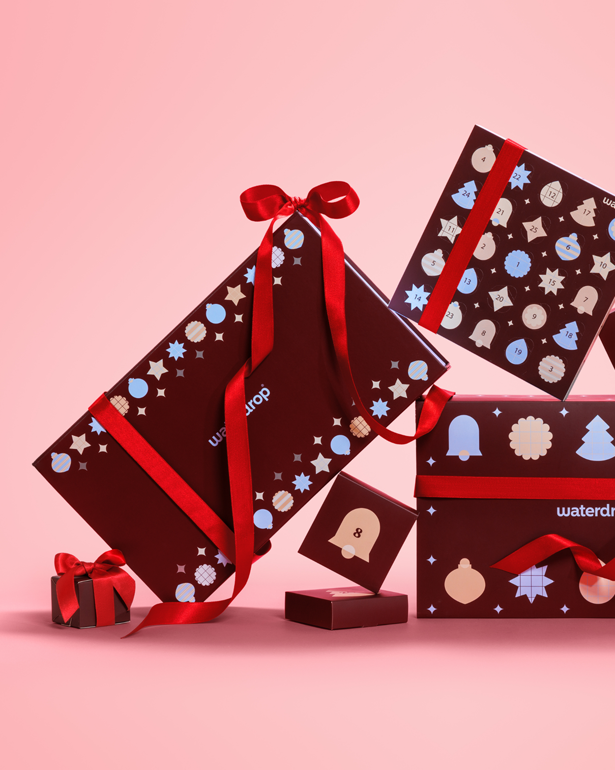 Cajas de regalo envueltas con lazos rojos y patrones festivos sobre un fondo rosa.