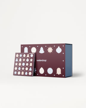 Calendario de Adviento con paneles morados y adornos navideños blancos, acompañado de una caja azul en el interior.