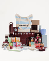 Conjunto de regalo con productos en cajas y envases variados dispuestos alrededor de una bolsa rayada.