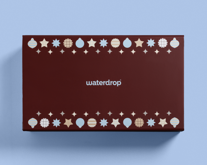 Caja rectangular color burdeos con formas circulares decorativas en los bordes superior e inferior sobre una superficie azul clara.
