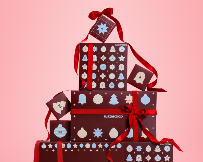 Pila de cajas de regalo decoradas con estampados y lazos rojos sobre fondo rosa.