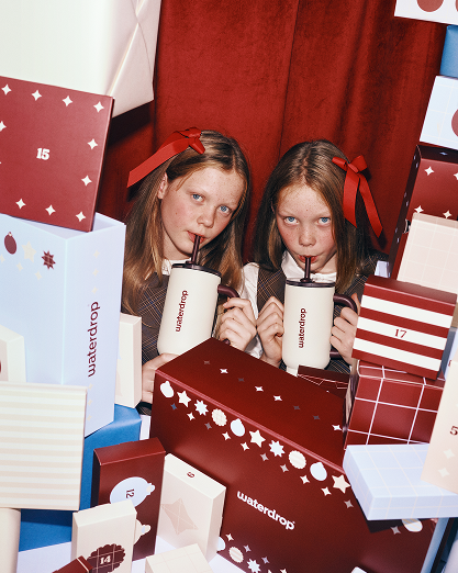 Dos niñas beben de vasos blancos entre regalos coloridos.