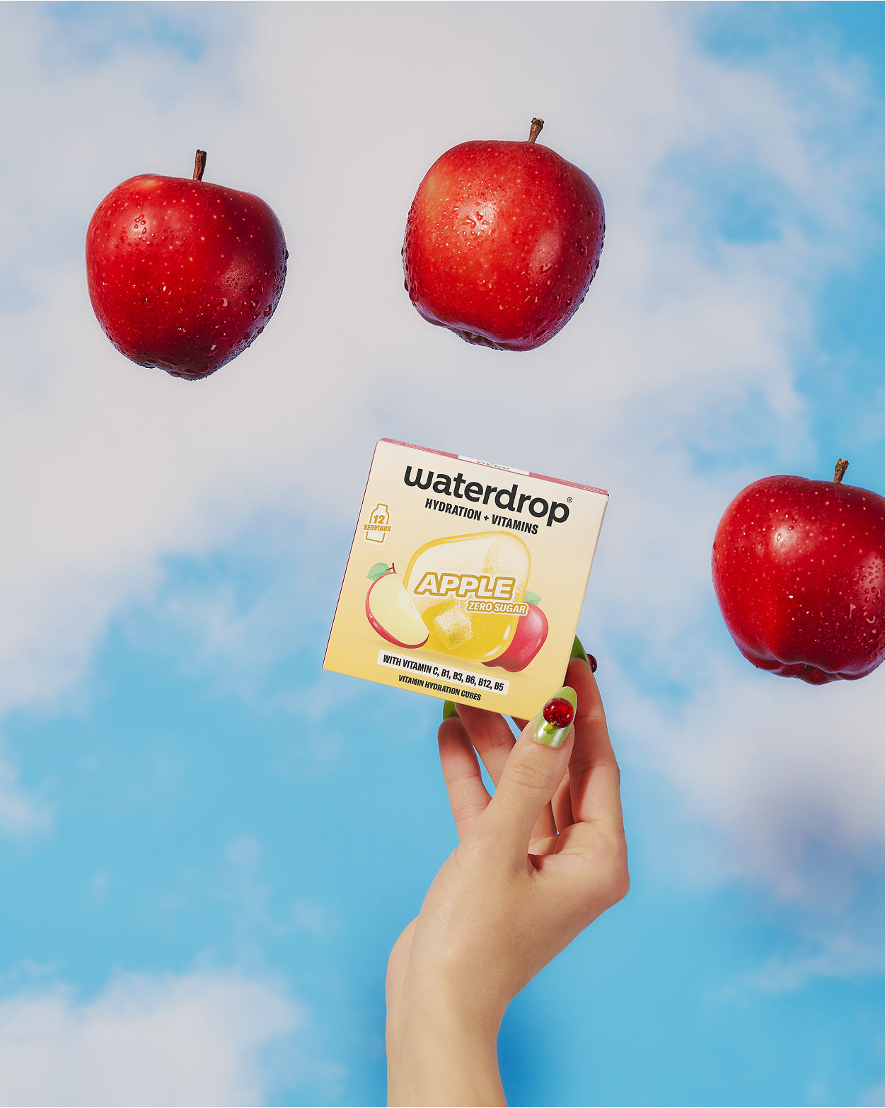 Mano sosteniendo una caja pequeña con una ilustración de manzana, fondo azul con tres manzanas rojas flotando.