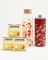 Conjunto de potenciadores de sabor para bebidas con cajas de manzana, una botella de vidrio con fruta y un vaso rojo con salpicaduras.