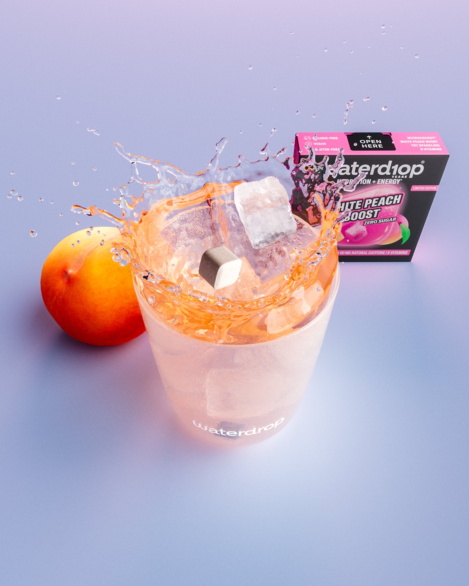 Vaso con bebida de durazno y cubos de hielo, un durazno y una caja al fondo.