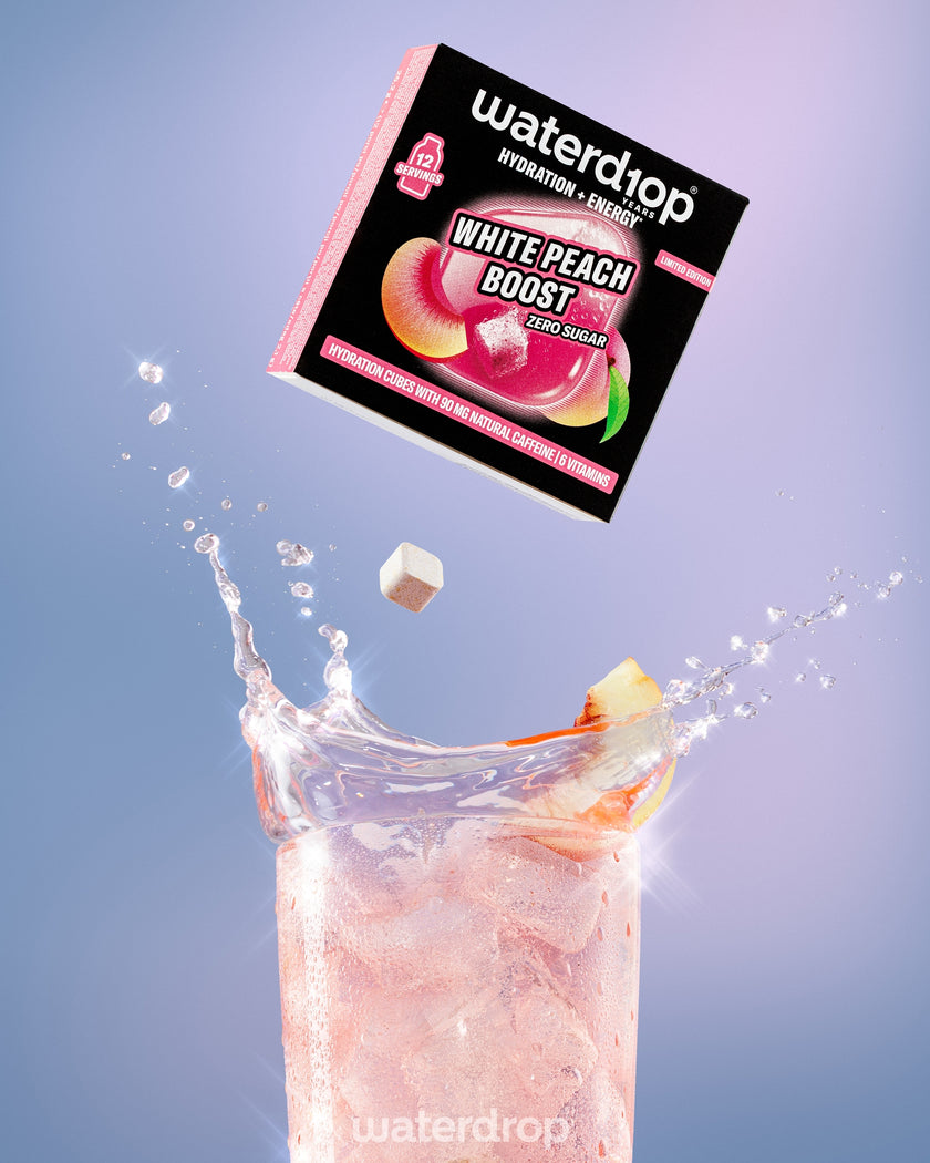 Paquete que cae hacia un vaso alto con bebida rosa de durazno y trozos de durazno, formando una salpicadura.
