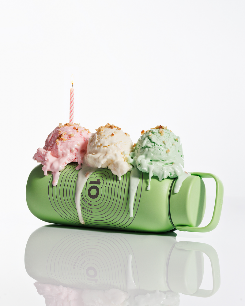 Taza verde inclinada con tres bolas de helado encima y una vela encendida, con glaseado derretido que gotea.