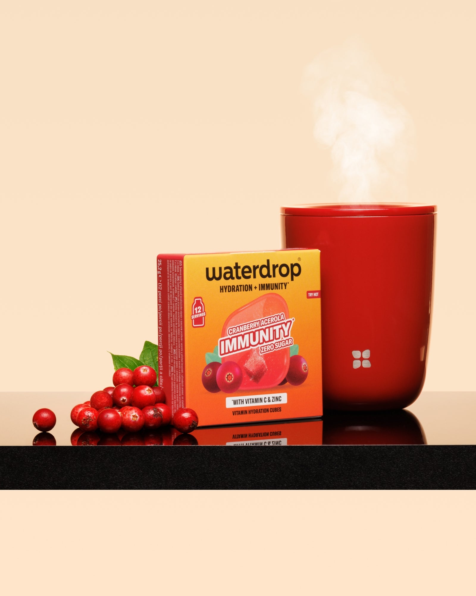Taza roja humeante junto a una caja roja y un racimo de arándanos sobre una superficie brillante.