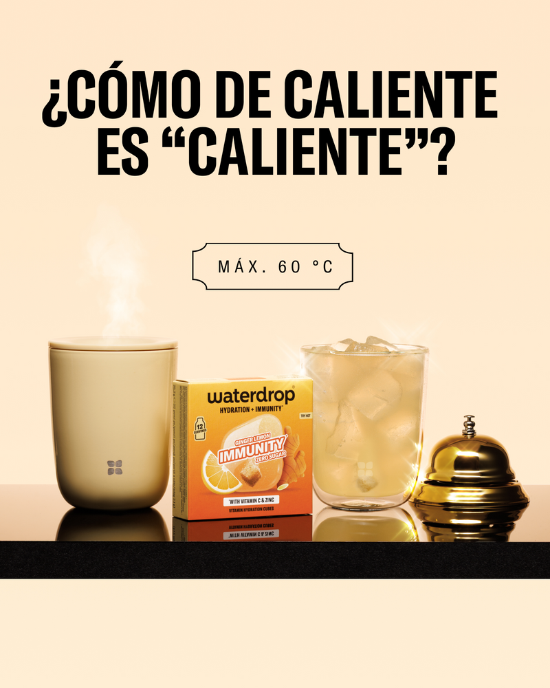 Configuración de bebida caliente con una taza humeante, una caja de inmunidad, un vaso con hielo y una campana de latón en una estantería oscura.