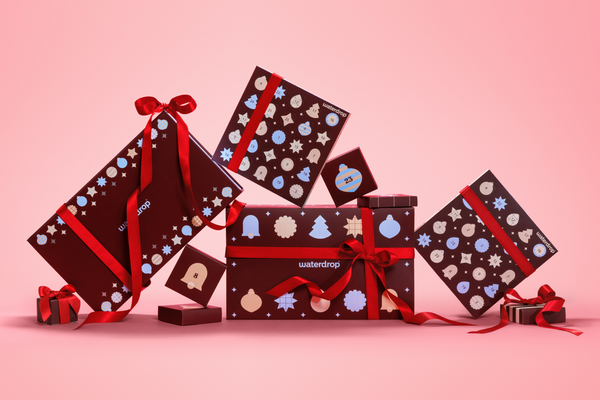Cajas de regalo envueltas con papel oscuro y lazos rojos sobre fondo rosa degradado.