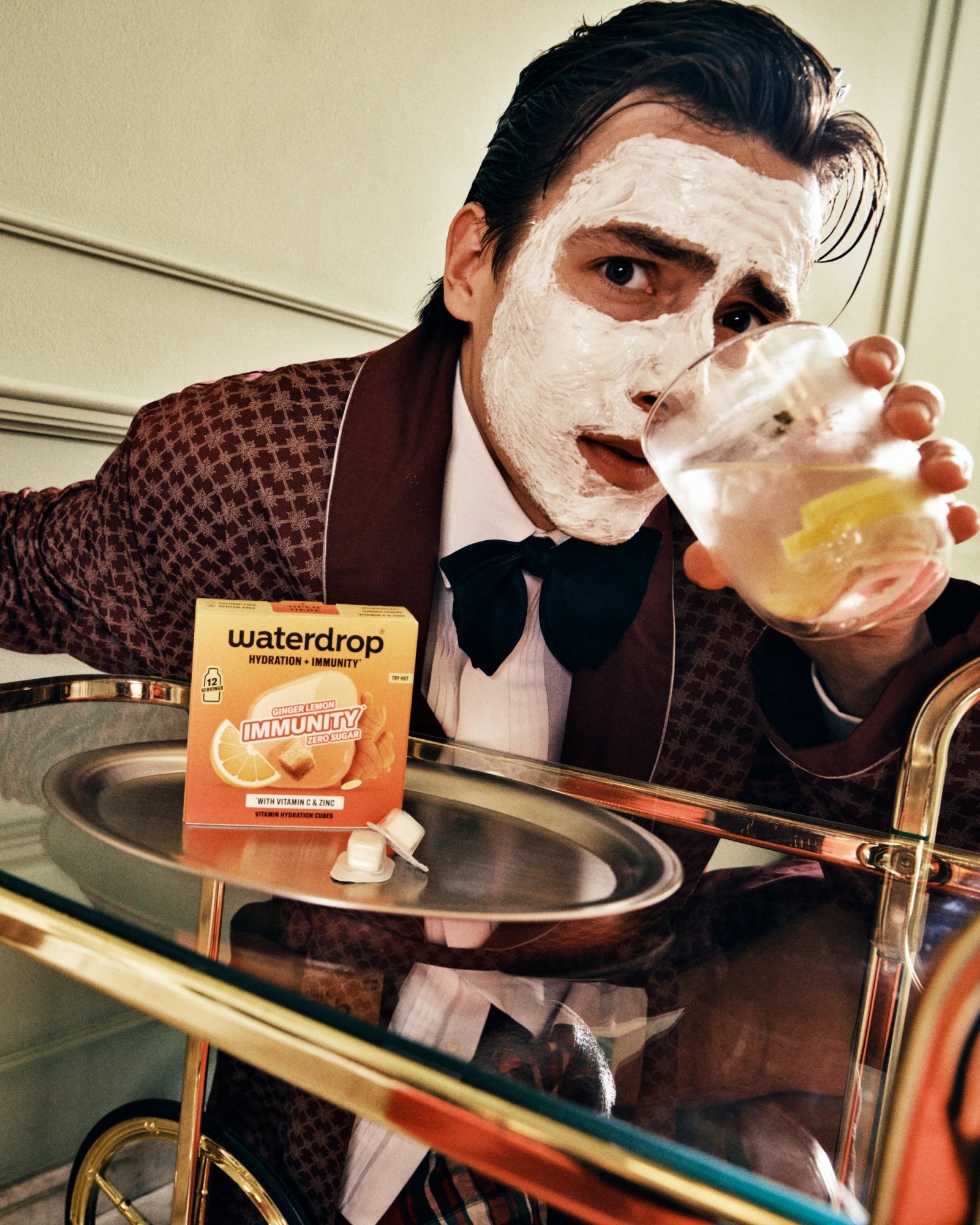 Hombre con traje marrón usando una mascarilla facial y bebiendo de un vaso en una barra.