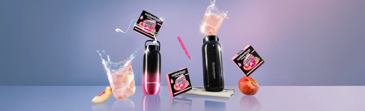 Conjunto de botellas negras con líquido rosado y pequeñas cajas de producto esparcidas sobre una superficie azul pastel.