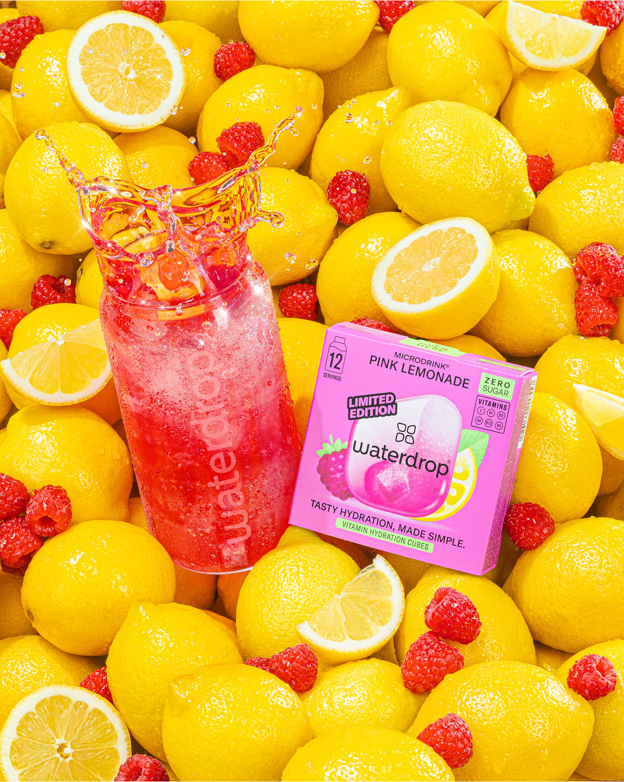 Botella de limonada rosa y una caja Waterdrop entre limones brillantes.