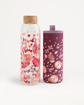Dos botellas de agua con patrón floral, una transparente con tapa de madera y otra morada con funda floral.